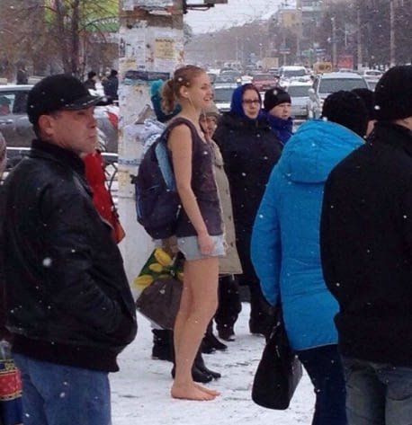 საზოგადოებრივი ტრანსპორტის მოლოდინში ჩაცმული ლამაზი გოგო თოვლში ფეხსაცმლის გარეშე დგას